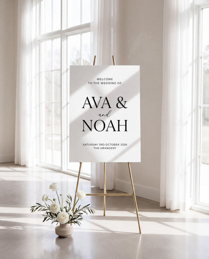 Personalized wedding welcome sign on gold easel in bright indoor venue with floral arrangement