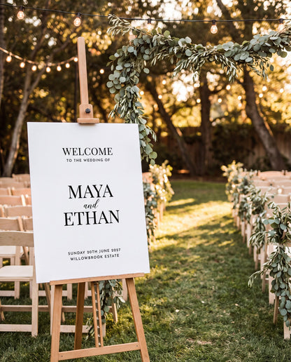 Custom wedding welcome sign displayed at outdoor ceremony aisle entrance with string lights