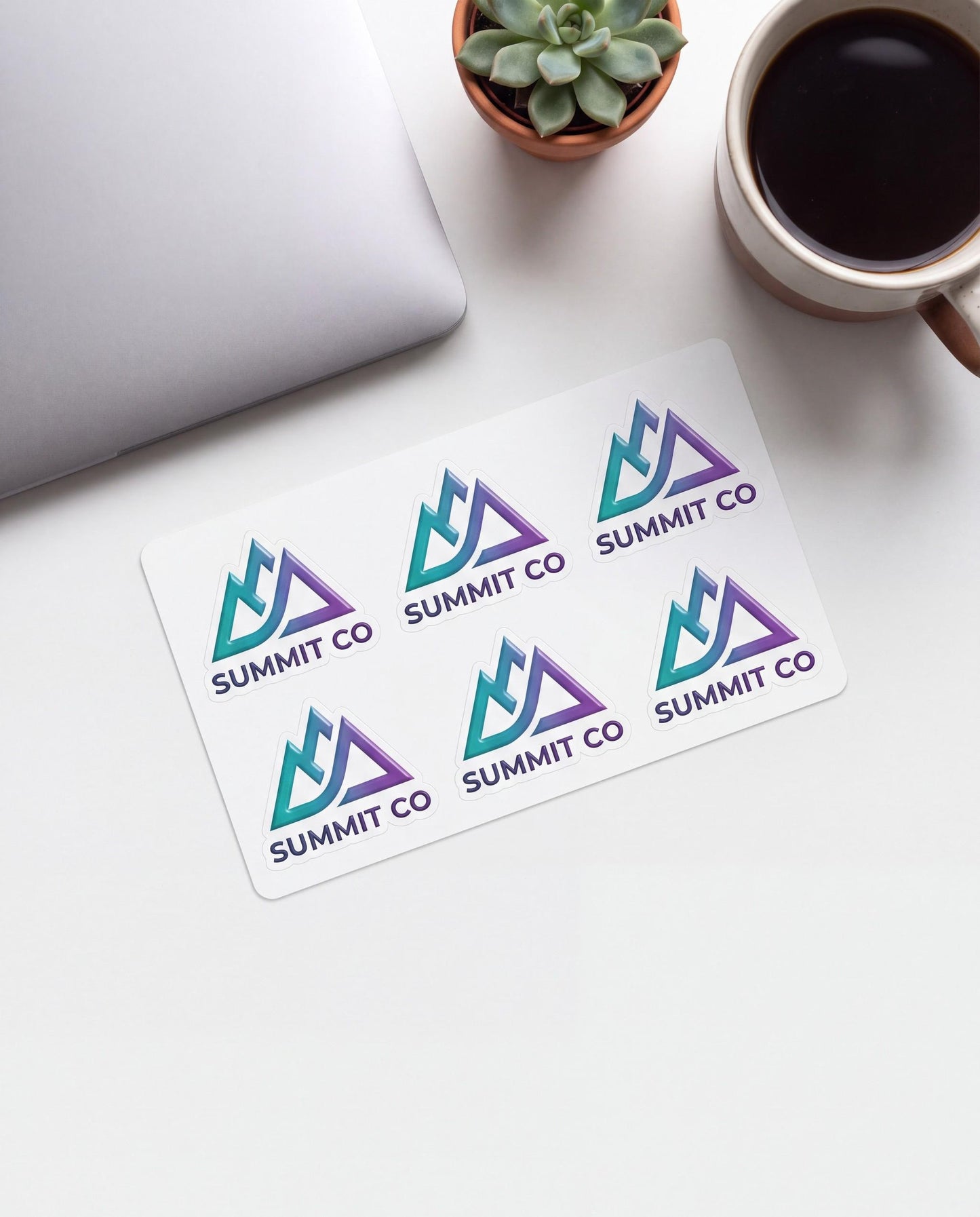 Flat lay of a kiss cut sheet of six custom logo stickers next to a laptop and coffee