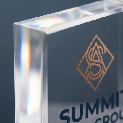 Close-up of acrylic logo block corner showing copper monogram logo and beveled glass edge