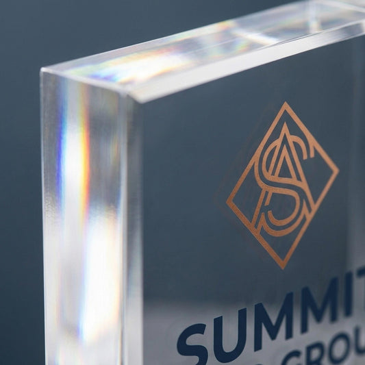 Close-up of acrylic logo block corner showing copper monogram logo and beveled glass edge