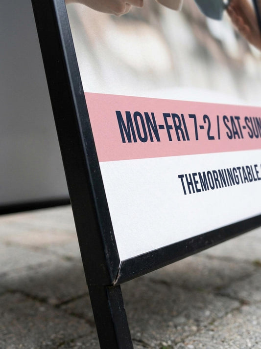 Close-up of sandwich board sign showing printed business hours and website text
