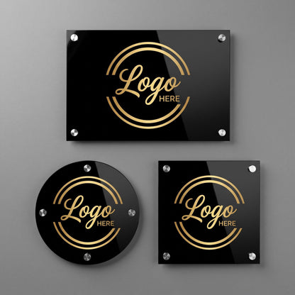 Three black acrylic logo plaques with gold circular emblem design and standoff mounts on a gray wall