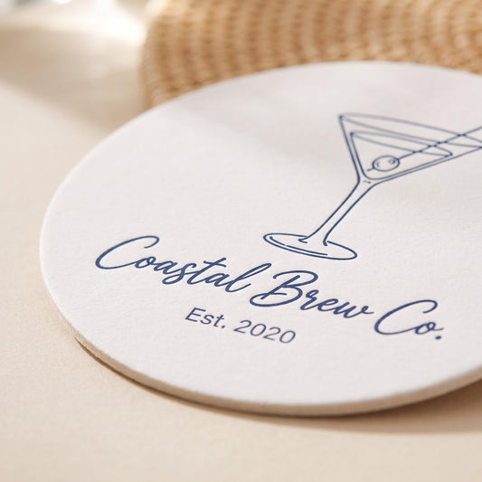 Close-up of a single custom logo coaster showing the crisp navy martini illustration and personalized business name and year text.