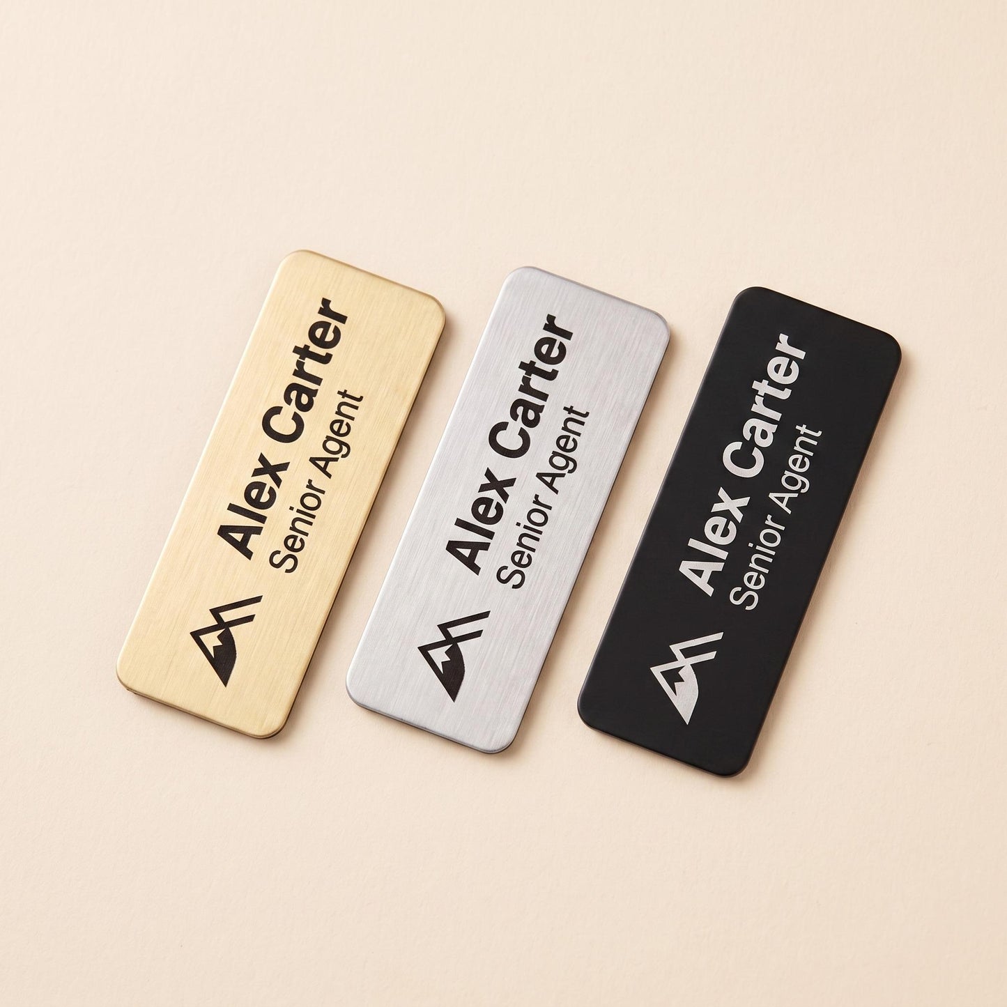 Three name badge color options shown side by side: brushed gold, brushed silver, and matte black.