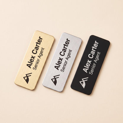 Three name badge color options shown side by side: brushed gold, brushed silver, and matte black.