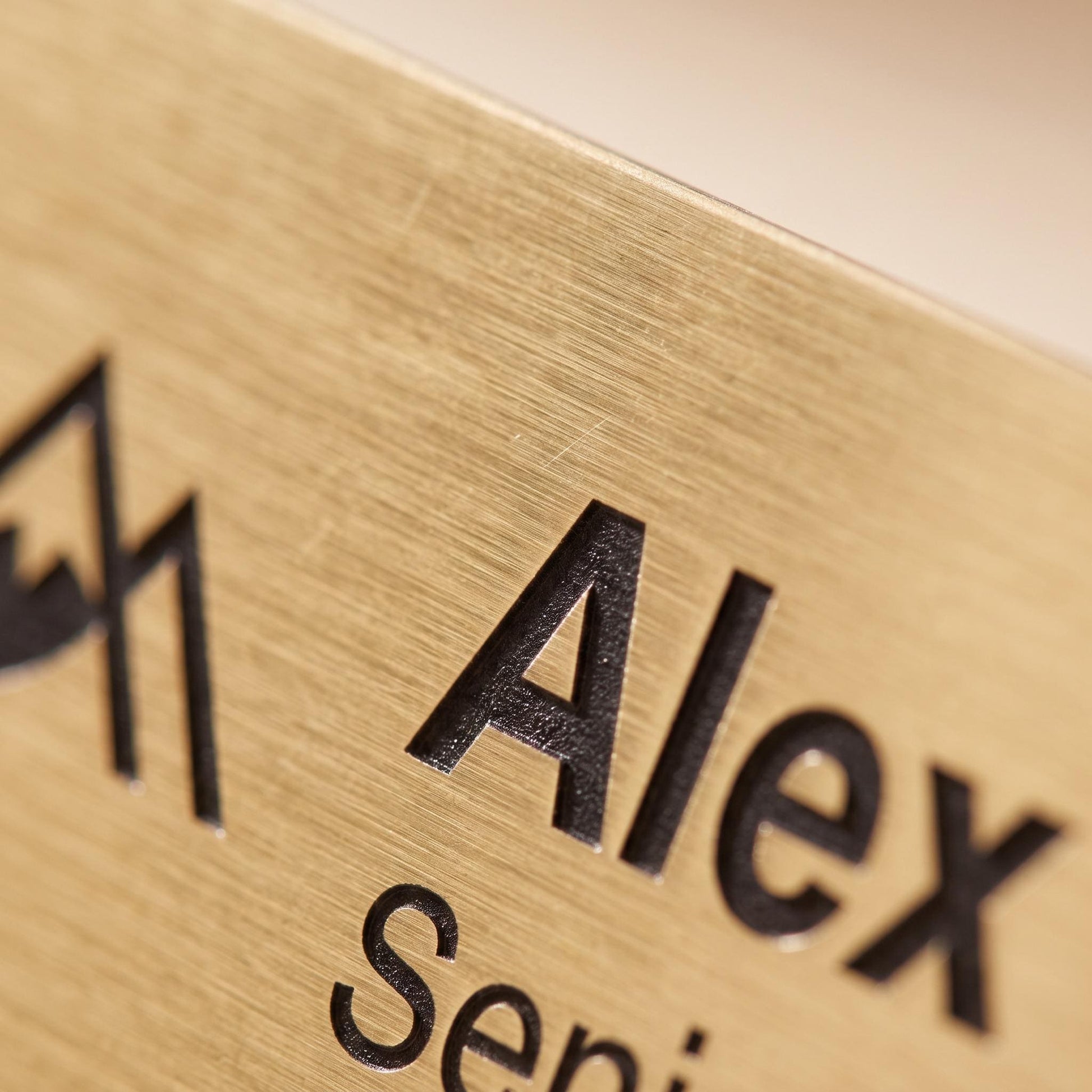 Close-up of the brushed-gold name badge showing the fine metal texture and crisp engraved text edge.