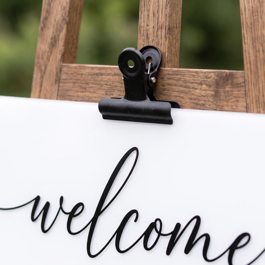 Close-up of the acrylic welcome sign showing the cursive welcome script and the easel wood grain and clamp.