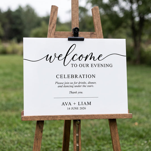 White acrylic welcome sign clipped to a wood easel outdoors, printed with custom cursive welcome text and event details.