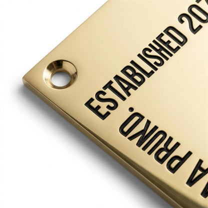 Macro close-up of deeply engraved black-infilled lettering on polished brass nameplate corner showing mounting hole and beveled edge