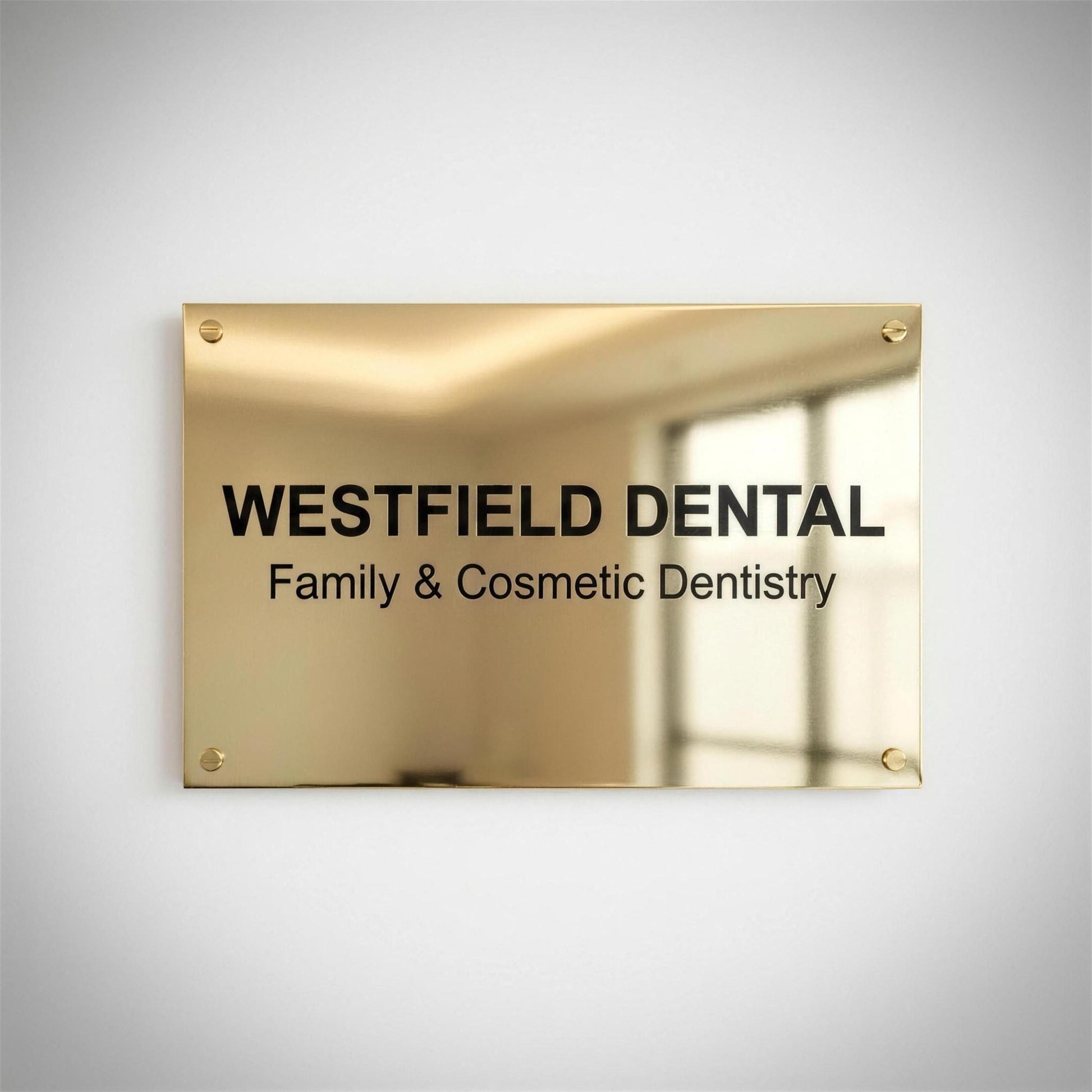 Polished brass business sign mounted on wall reading Westfield Dental Family and Cosmetic Dentistry, frontal reflective shot