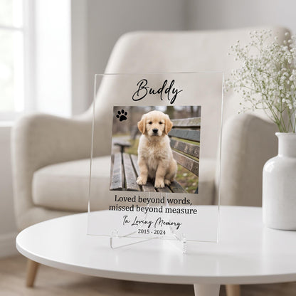Clear acrylic pet memorial plaque with a printed puppy photo, pet name, memorial verse, and dates, displayed on a stand on a white table.